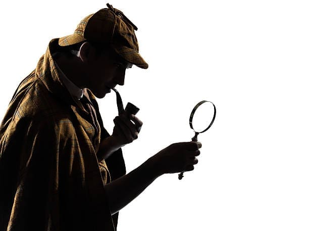 a man in a hat and coat holding a magnifying glass Private Investigator Los Angeles Rates